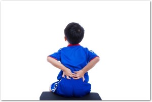 Back pain. Athlete little asian (thai) boy in blue sportswear sitting and rubbing the muscles of his lower back, cropped torso portrait, isolated on white background. Studio shot